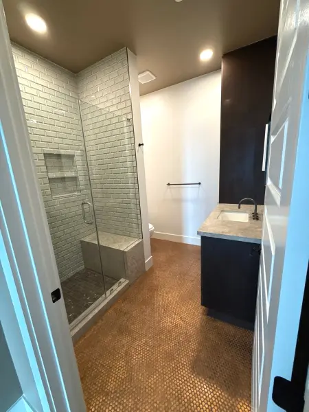 Completed bathroom renovation showing penny-tile flooring, subway-tile shower enclosure with glass door, dark vanity with marble countertop, and recessed lighting in Austin, TX.
