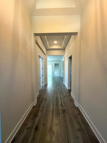 Clean, finished hallway with dark wood-look vinyl flooring, cream-colored drywall, white trim, and a modern gray coffered ceiling with recessed lighting in Briarcliff, TX.