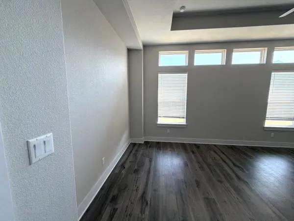 Finished interior room with freshly painted drywall, new dark wood-look flooring, white trim, and multiple windows with shutters in Briarcliff, TX.