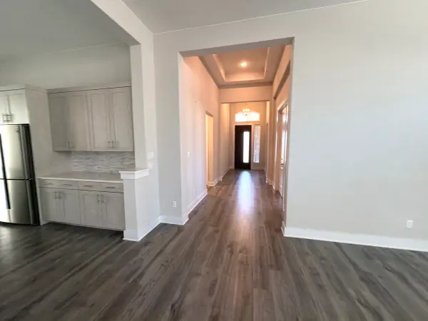 Clean, finished interior space showing newly installed dark wood-look flooring, freshly painted white walls and ceiling, open-concept kitchen and hallway with modern finishes and warm lighting in Briarcliff, TX.