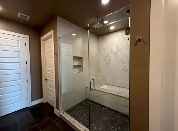 Completed master bathroom with large walk-in shower enclosure, marble-look surround, dark tile floor, recessed lighting, and white cabinetry in Austin, TX.