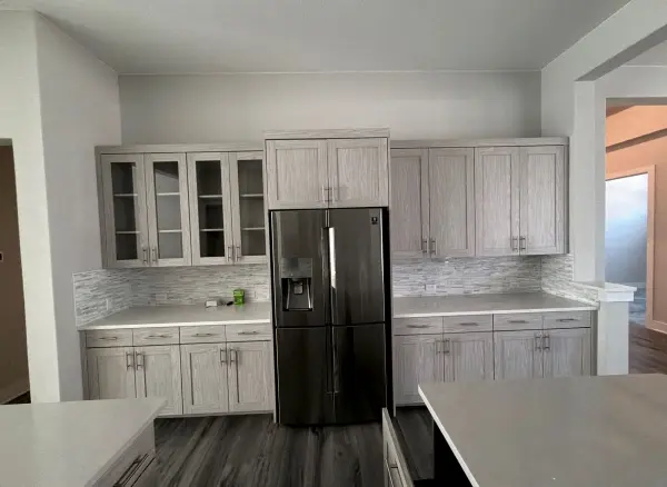 Completed kitchen renovation showing light gray cabinetry, marble backsplash, white countertops, and black stainless steel refrigerator in Briarcliff, TX.