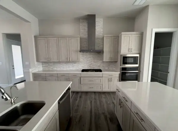 Completed modern kitchen with light wood cabinetry, white quartz countertops, subway tile backsplash, stainless steel appliances, and dark wood-look flooring in Briarcliff, TX.