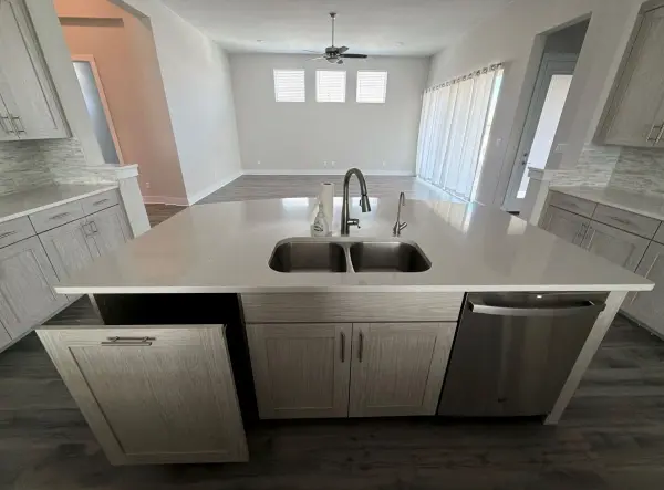 Finished kitchen with white cabinetry, light gray quartz countertops, black dual sink with faucet, stainless steel dishwasher, and light wood-look flooring in Briarcliff, TX.