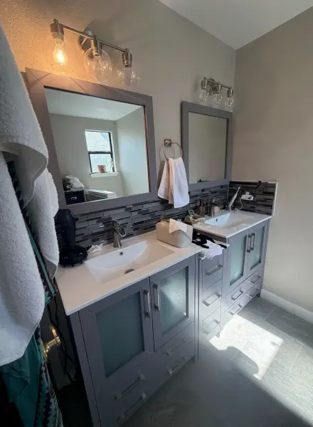 Completed master bathroom renovation with dual vanities, dark tile backsplash, vessel sinks, mirror lighting fixtures, and new flooring in Austin, TX.
