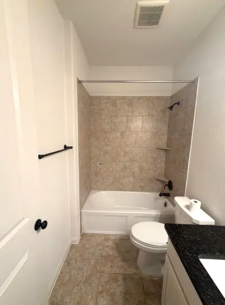 Freshly renovated bathroom with new tile surround, black hardware, white vanity, and towel bars installed in Austin, TX.