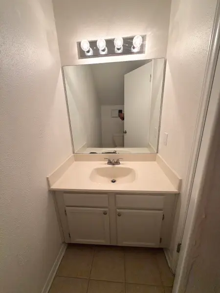 Completed bathroom vanity with four-light mirror fixture, white cabinet sink, and tile flooring in Austin, TX.