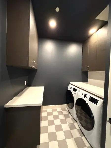 Newly renovated laundry room with dark walls, white quartz countertops, recessed lighting, tile flooring, and side-by-side white washers and dryers in Austin, TX.