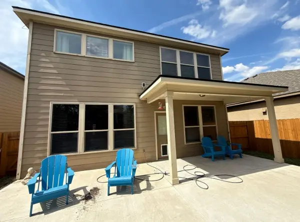 Completed patio and covered pergola addition with blue Adirondack chairs on concrete pad in front of modern residential home in Austin, TX.