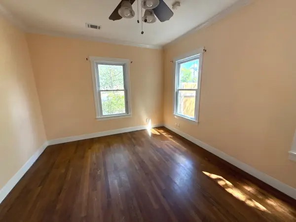 A freshly painted bedroom with cream-colored walls, white trim, dark hardwood flooring, and two windows with natural light in Austin, TX.