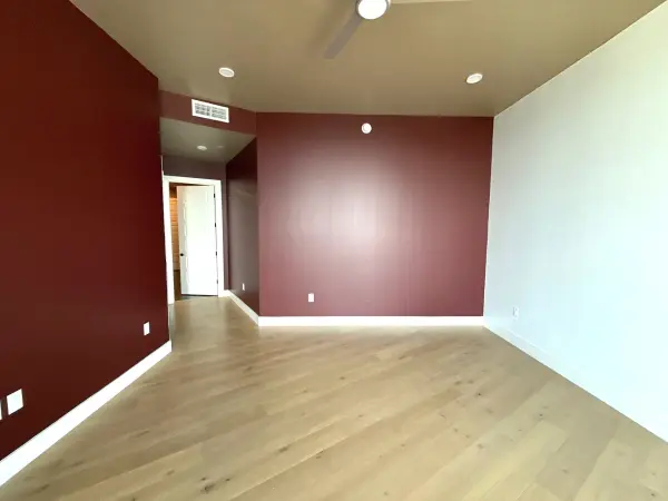 Finished interior room with deep burgundy accent wall, light mint green wall, recessed ceiling lights, white trim, and newly installed light wood-tone laminate flooring in Austin, TX.