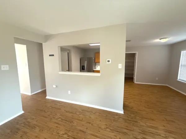 Clean, newly painted living room and kitchen pass-through with fresh drywall and white trim, wooden flooring, and neutral walls in Leander, TX.